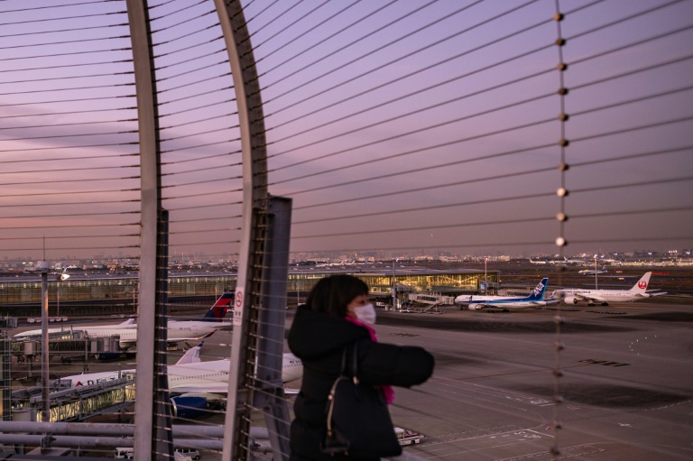 Un voyageur observe des avions sur la piste de l'aéroport international de Haneda, le 29 novembre 2021 à Tokyo (AFP - Philip FONG)