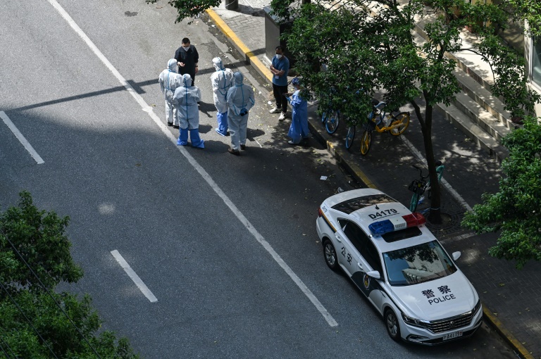 Une voiture de police et des fonctionnaires en tenue de protection Covid-19 complète dans une zone réglementée de Shanghai, le 8 mai 2022 (AFP - Hector RETAMAL)