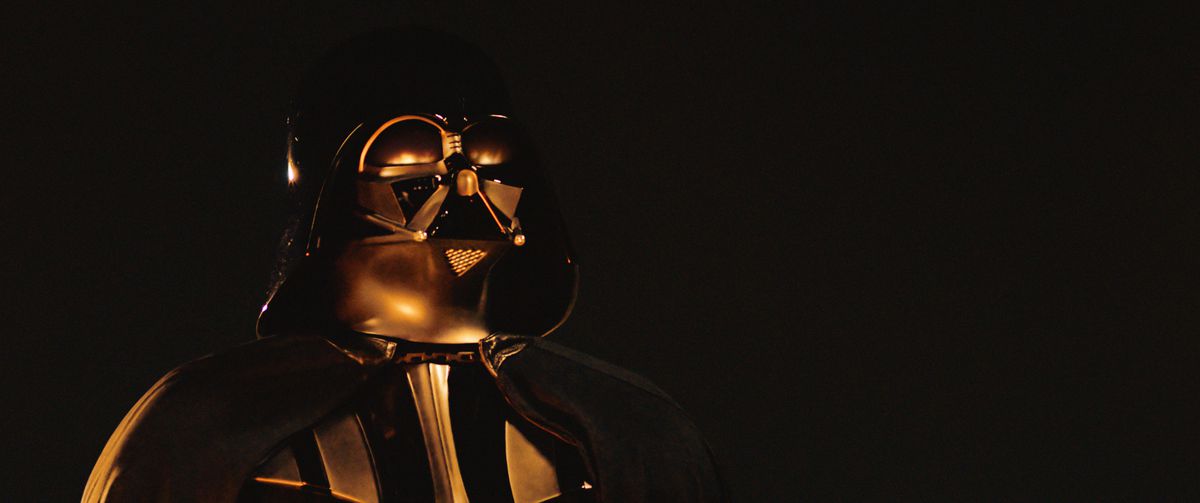 Un Dark Vador masqué (Hayden Christensen) est illuminé par des flammes sur un fond sombre dans Obi-Wan Kenobi.