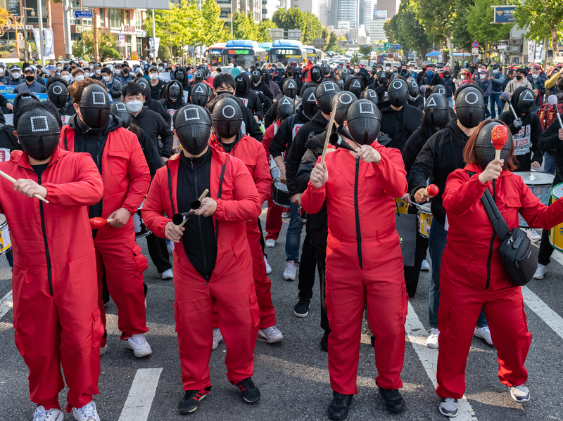 Les membres de la Confédération coréenne des syndicats portent des masques costumés dans la série Netflix Squid Game pour une marche vers l'hôtel de ville de Séoul lors d'un rassemblement contre la politique du travail du gouvernement le 20 octobre 2021 à Séoul, en Corée du Sud.