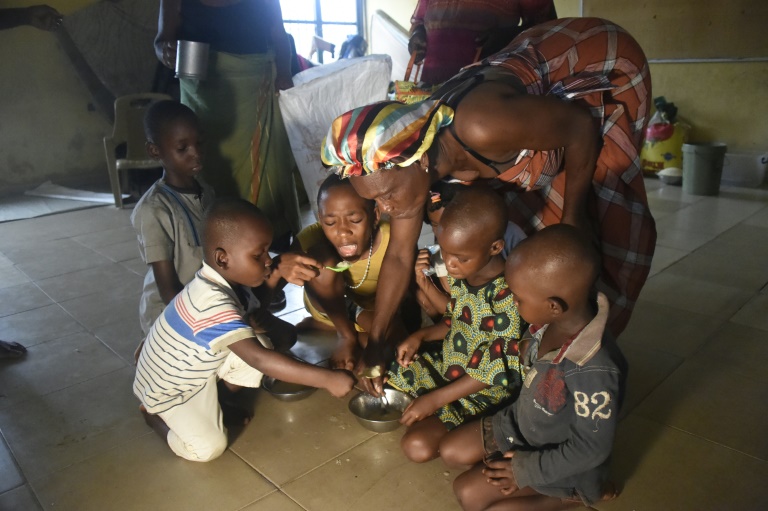 Une mère et ses enfants mangent dans un camp de personnes déplacées le 21 octobre 2022 à Iuika, dans la région inondée d'Ahoda, dans le sud du Nigeria.  (AFP - PIUS UTOMI EKPEI)