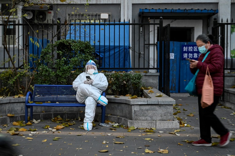 Un homme vêtu d'une combinaison de matières dangereuses est assis devant un complexe d'appartements en détention en raison du Covid-19 à Pékin, le 22 novembre 2022. (AFP - Jade GAO) #