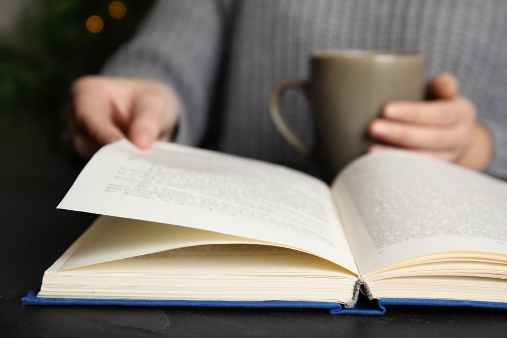 Femme,avec,une,tasse,de,boisson,lisant,un,livre,à,une,table,,Closeup