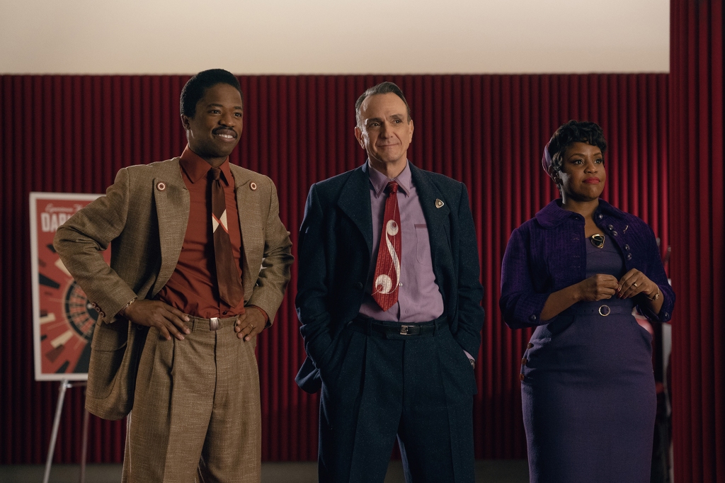 Le monde étrange de l'ère spatiale de la série steampunk "Hello, Tomorrow !". 5 Dewshane Williams, Hank Azaria et Haneefah Wood dans une scène de "Hello, World !" Ils sont debout l'un à côté de l'autre et regardent quelqu'un d'autre ; Dewshane a les mains sur ses hanches et Hank a les mains dans sa poche. Ils portent tous des tenues de type années 50 (des costumes pour les hommes et une robe pour Haneefah).