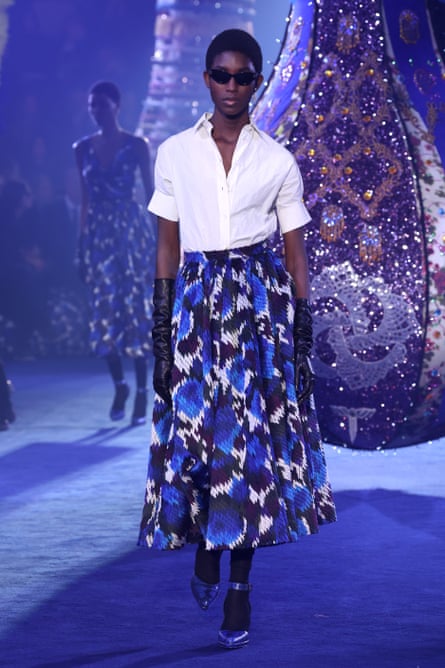 Dior revient dans les années 1950 avec l'ouverture de la Fashion Week de Paris | Dior 1 Mannequin sur le podium portant une chemise à col blanc, une jupe bleu imprimé style New Look, des gants d'opéra noirs.